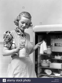 1930s-woman-wearing-a-white-apron-taking-milk-out-of-the-refrigerator-AAM1RN